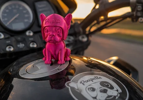 Une figurine Poupette posée sur un réservoir de moto, au coucher du soleil