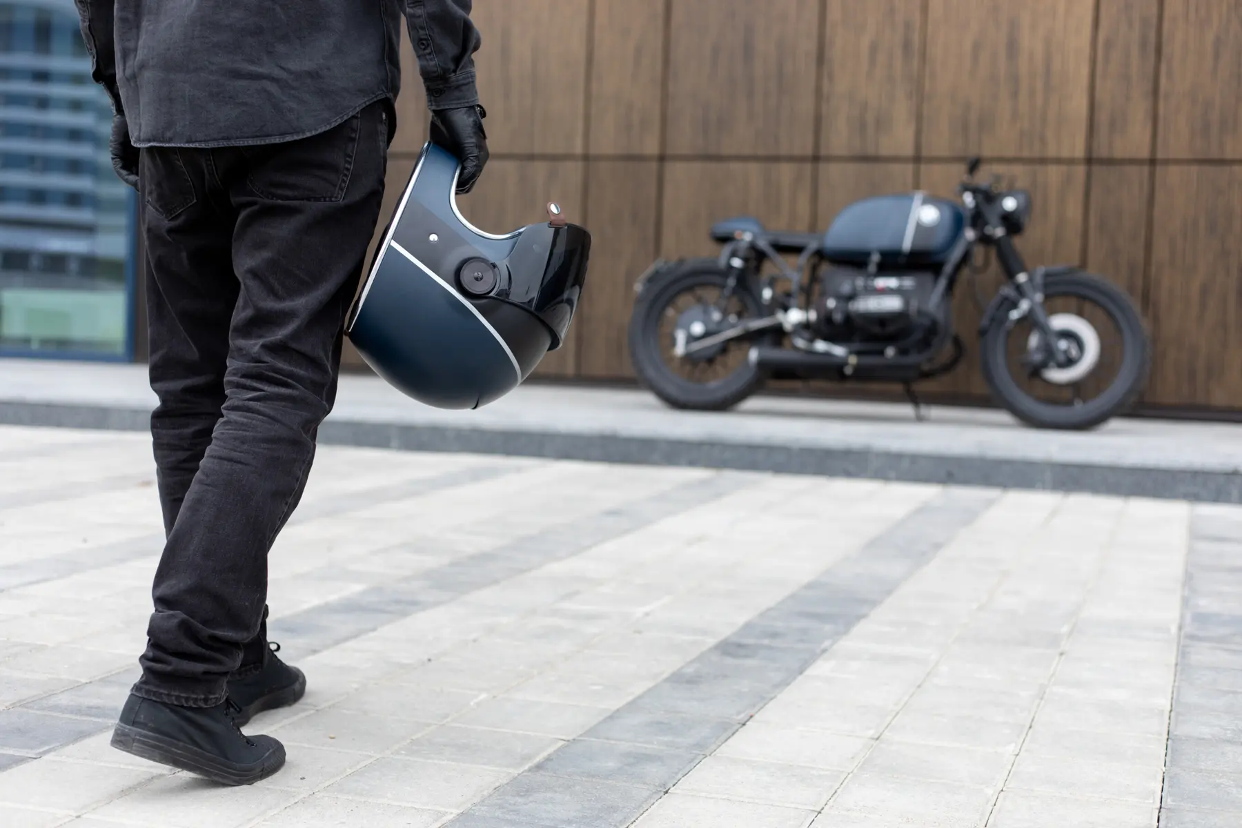 Un motard tenant son casque, sa moto à l'arrière-plan