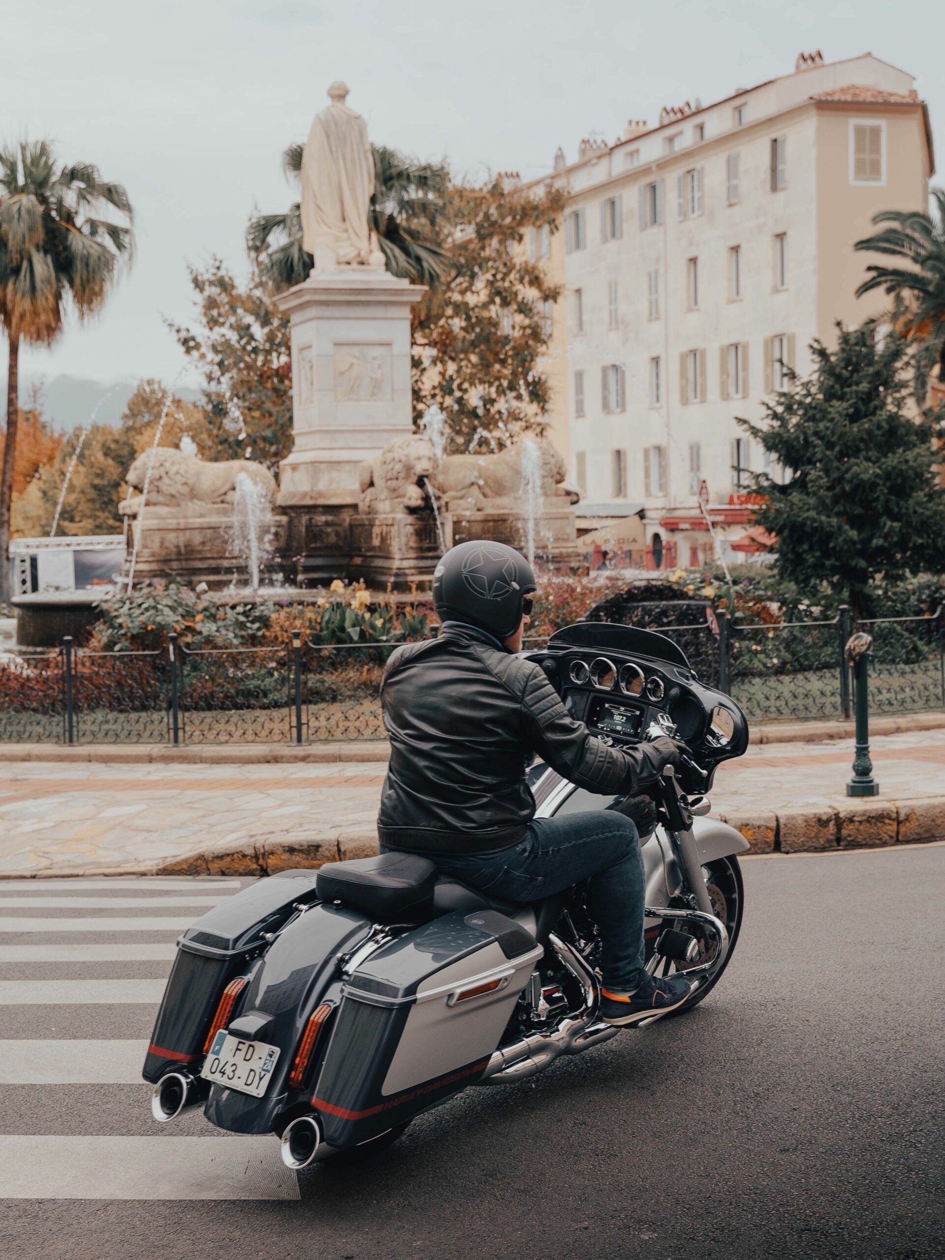 Moto traversant une place du centre-ville d'Ajaccio, près de la statue et de la fontaine